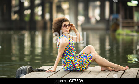 Young beautiful Asian woman sits on a wooden river pier. Stock Photo