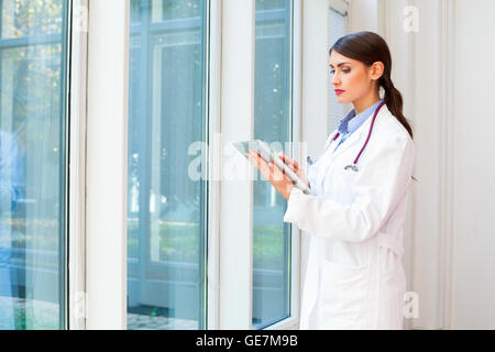 A photo of female doctor using digital tablet. Young medical professional is wearing lab coat. She is standing in hospital. Stock Photo