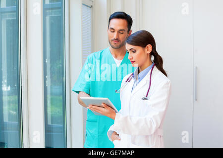 A photo of young medical team using digital tablet. Medical professionals are in uniforms. They are standing in hospital. Stock Photo