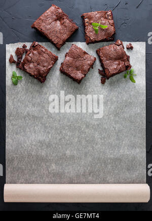 few pieces of brownies on baking paper  with space for information  (top view). black concrete background. dark Stock Photo