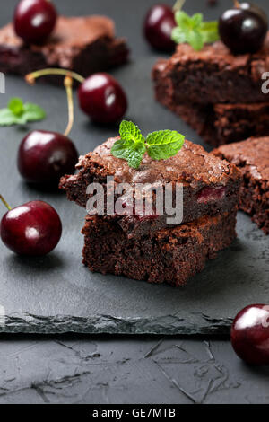few pieces of brownie with cherries and mint on a black concrete background Stock Photo