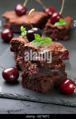 few pieces of brownie with cherries and mint on a black concrete background Stock Photo