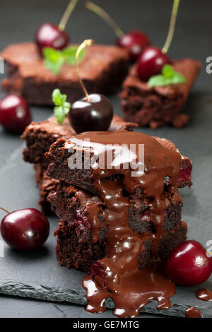 few pieces of brownie with cherries and with chocolate cream on a black concrete background Stock Photo