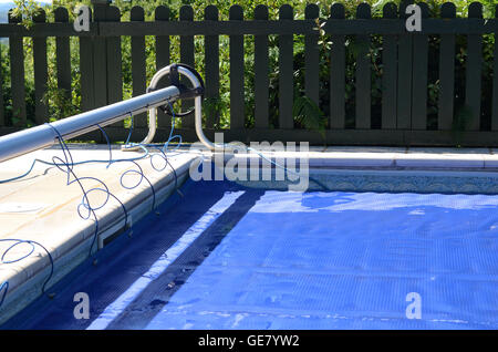 Swimming pool cover off its roller and covering the pool Stock Photo