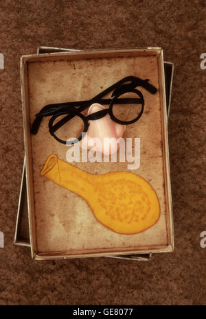 Joke false nose with plastic spectacles and eyebrows attached lying in box with old yellow balloon Stock Photo