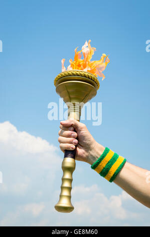 Hand of torchbearer Brazilian athlete wearing Brazil colors sweatband holding sport torch against tropical blue sky Stock Photo