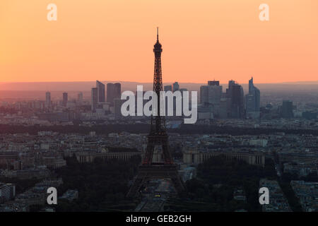 The sun sets behind the Eiffel Tower and the skyscrapers of La Defense business district in Paris, France. Stock Photo