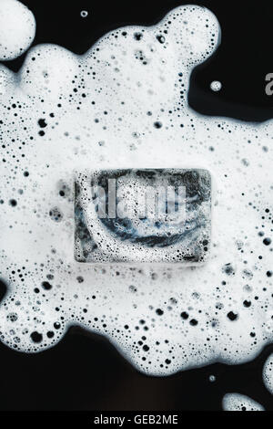 Black coal soap in foam on black background. Close-up composition. Top view. Stock Photo
