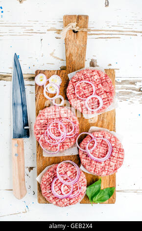 Raw ground beef meat cutlet for making burgers with onion rings and spices on wooden board over white backgroun Stock Photo