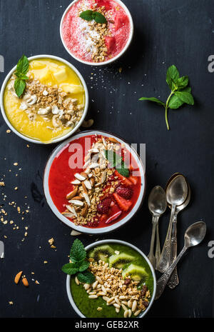 Healthy summer breakfast concept. Colorful fruit smoothie bowls with nuts and oat granola on black background Stock Photo