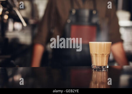 Shot of cup of coffee on counter with barista standing in background. Stock Photo