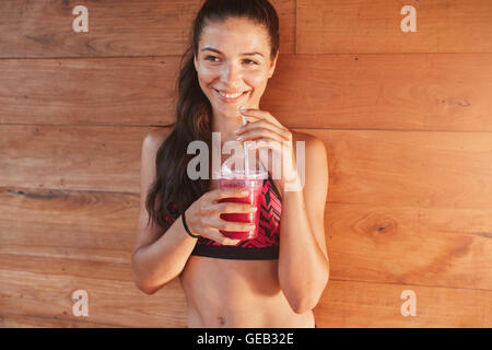 Portrait of smiling young woman drinking fruit juice over wooden background. fitness female in sportswear having juice after wor Stock Photo