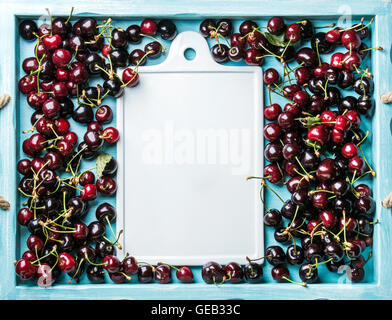 Sweet cherries in blue wooden tray with white ceramic board in center Stock Photo