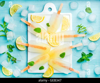 Lemonade popsicles with lemon slices, fresh mint leaves and ice cubes on white ceramic board Stock Photo