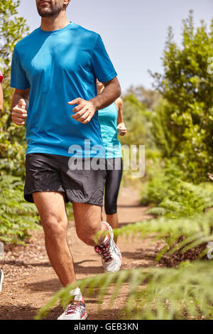 Two young joggers out for a run on a gravel path surrounded by bushes, wearing casual running clothes in the late morning sun Stock Photo