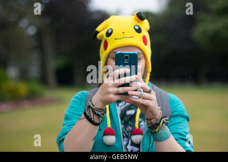 A girl holds her mobile phone while playing Pokemon Go while wearing a Pokemon Pikachu hat. Stock Photo