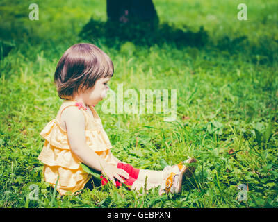 One-year baby girl sitting on grass and looking away Stock Photo