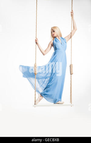 Blonde ballerina in blue dress on swings Stock Photo