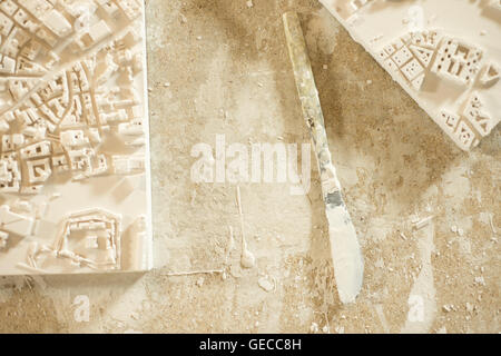 A plaster-coated knife placed between two 3D city map plaster models on plaster-splattered wooden table top. Stock Photo