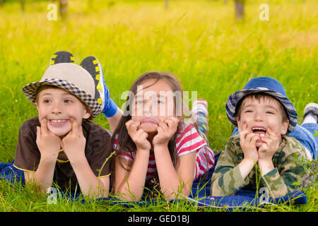 Three happy kids sitting on grass in summer day Stock Photo