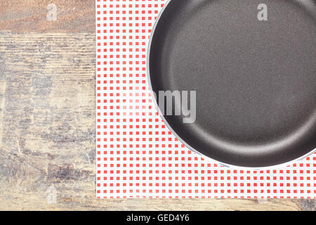 Top view of new empty frying pan on a napkin and wooden table, kitchen background. Stock Photo