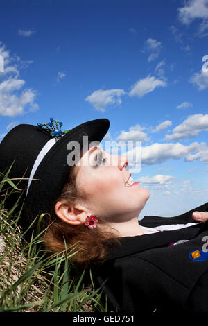 Beautiful young woman laying in the grass looking up at blue sky with clouds Stock Photo