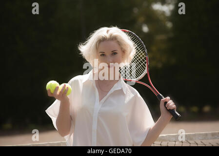 PORTRAIT OF A YOUNG TENNIS PLAYER.  A young female tennis player with fair hair holding a racquet and tennis balls Stock Photo