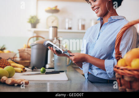 Female employee in a juice bar swiping a credit card in a card reader machine. African woman standing at checkout counter. Stock Photo