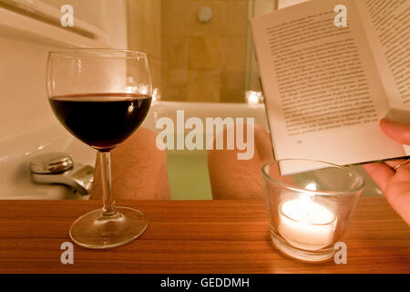 Man sitting in a bathtub, bathing, reading a book, drinking wine, candles, spa, relaxing Stock Photo