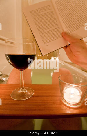 Man sitting in a bathtub, bathing, reading a book, drinking wine, candles, spa, relaxing Stock Photo