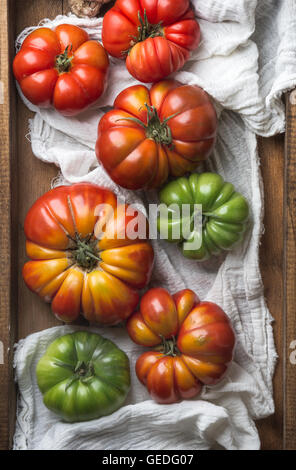 Colorful Heirloom tomatoes on white textile in rustic wooden tray, top view Stock Photo