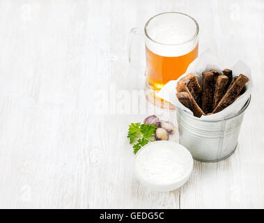 Beer snack set. Pint of pilsener in glass mug and rye bread croutons with garlic cream cheese sauce over white painted old wooden background Stock Photo