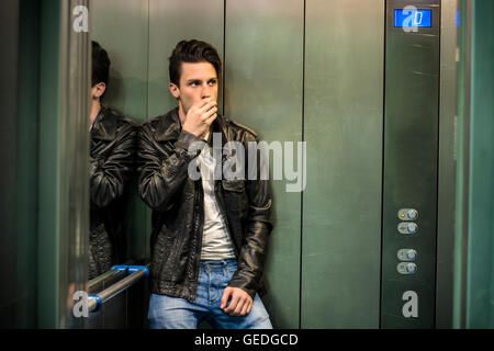 Scared young man desperate in stuck elevator screaming, looking very upset Stock Photo