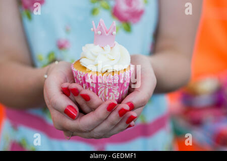 Close up shot of a womans hands holding a pretty cupcake. She is wearing a bright flower deisgn dress. The cupcake is pink and w Stock Photo