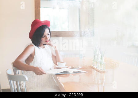 Woman in Red Hat Reading while Drinking Coffee Stock Photo