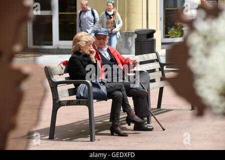 Man and woman couple sitting on public bench seat San Sebasti‡n Donostia Spain Stock Photo