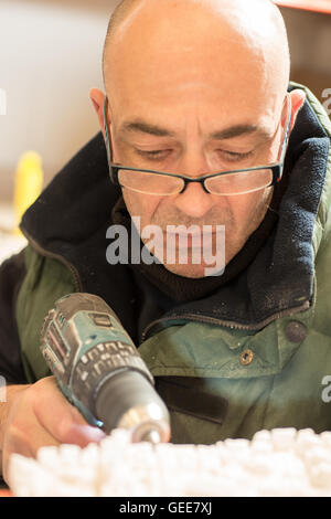 Man perforating a hole on the side of a plaster model using an electric drill. Stock Photo