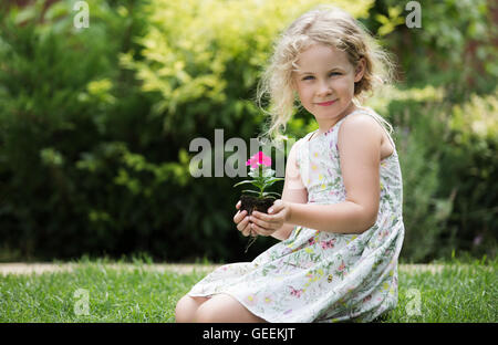 Little blonde girl holding young flower plant in hands on green background Stock Photo