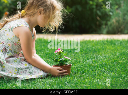 Little blonde girl holding young flower plant in hands on green background Stock Photo