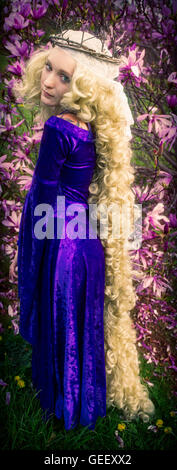 Young woman dressed as Rapunzel wearing purple velvet medieval costume with long, curly blond hair. Stock Photo