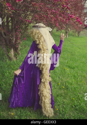 Young woman dressed as Rapunzel wearing purple velvet medieval costume with long, curly blond hair. Stock Photo