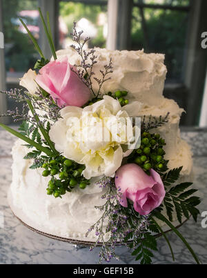 White wedding cake with white icing, roses, peonies, greenery Stock Photo
