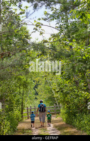 Mother with two small children hiking in a outdoor nature park  on field trip with parents in a group in fields and forest. Stock Photo