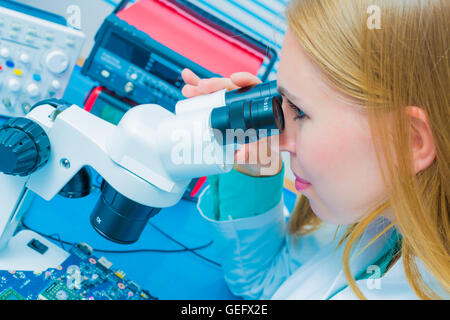 Blonde  young computer technician testing a printed circuit board with a microscope Stock Photo