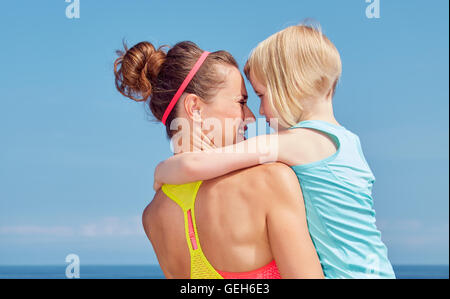 Look Good, Feel great! Seen from behind mother and child in fitness outfit hugging on embankment Stock Photo