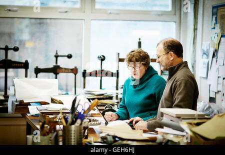 Two people working in a book binding business. Surrounded by tools and book presses. Stock Photo