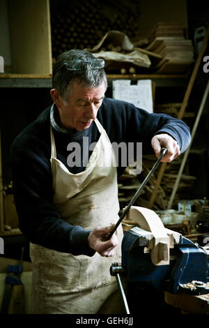 A man working in a furniture maker's workshop using a rasp on a wooden shape in a clamp. Stock Photo