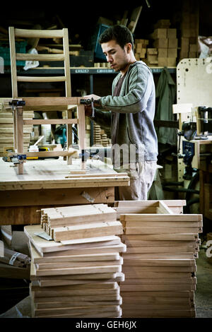 A man working in a furniture maker's workshop assembling a chair. Stock Photo
