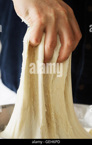 Close up of a baker kneading bread dough in a metal bowl. Stock Photo