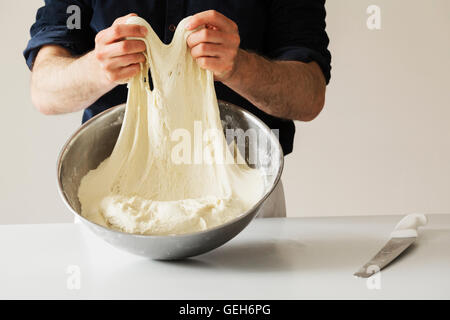 Close up of a baker kneading bread dough in a metal bowl. Stock Photo
